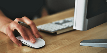 Hand on a mouse next to a Mac computer