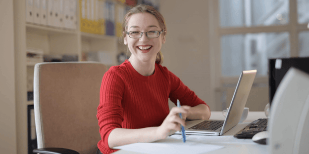 Lady wearing a red top sitting at a desk and smiling into the camera