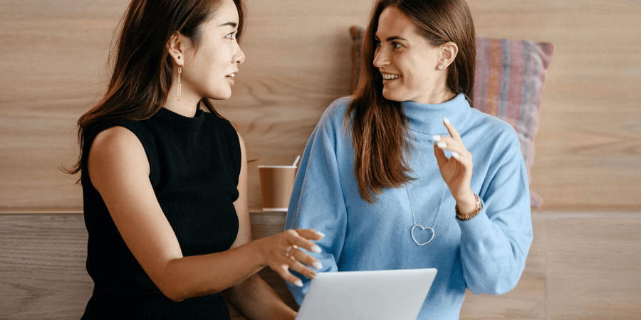 Two women in conversation with a laptop open in the middle between them