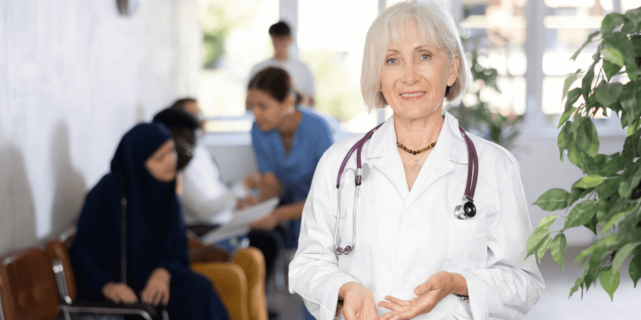 Older female doctor standing in front of a busy waiting room